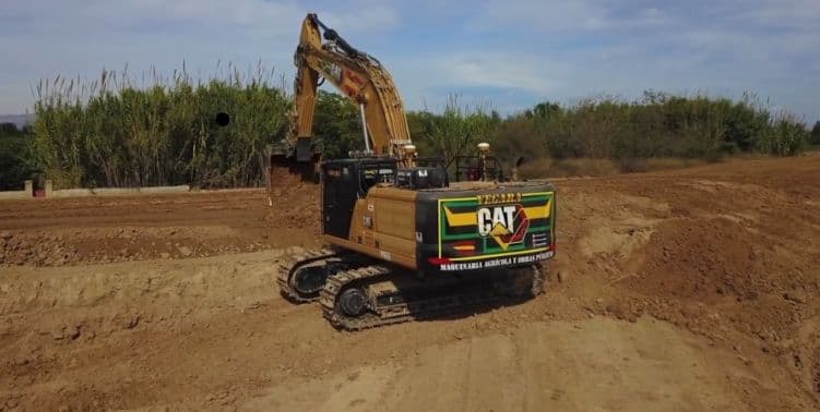 Excavadora Caterpillar rotulada Vegara excavando en una parcela junto a un cañaveral