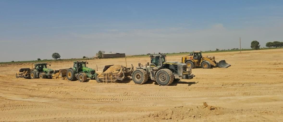 Cuatro máquinas de Tractores Vegara paradas en una parcela recién nivelada: tres tractores John Deere con traílla y una cargadora Caterpillar