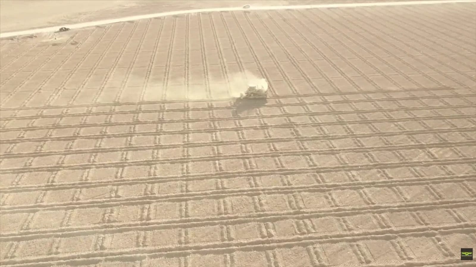 Vista aérea de la parcela con la máquina trabajando y la estela de polvo, y el camino de servicio al fondo