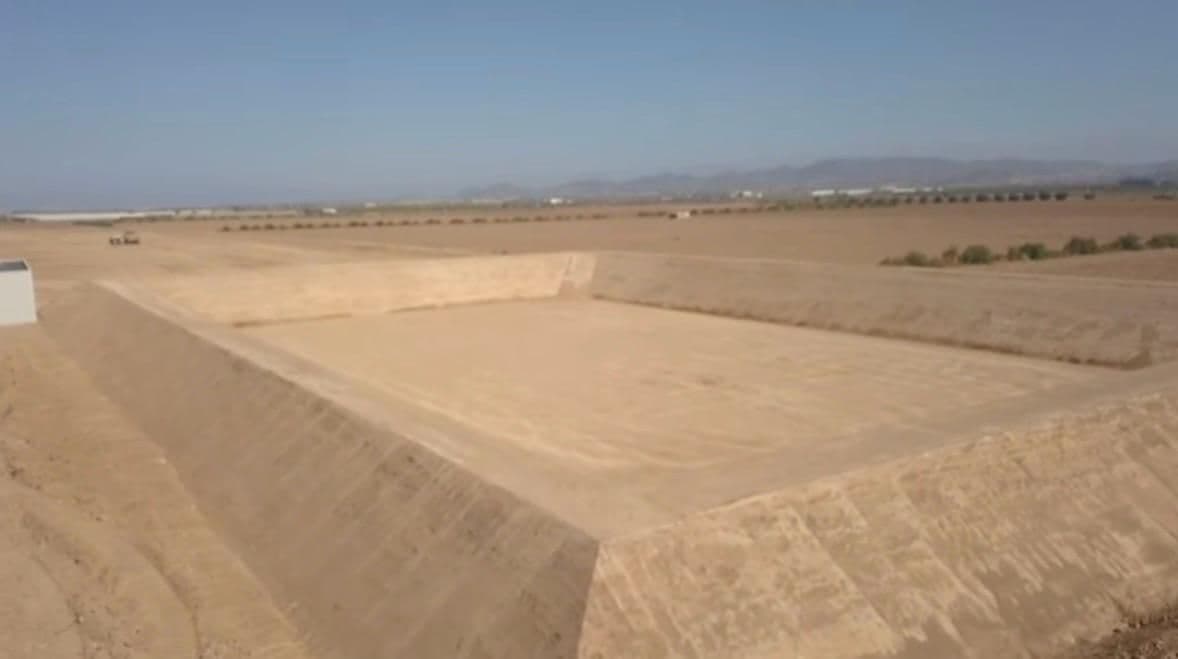 Plano amplio de la balsa acabada, con el fondo compactado, el talud de poniente a la sombra y la sierra al fondo
