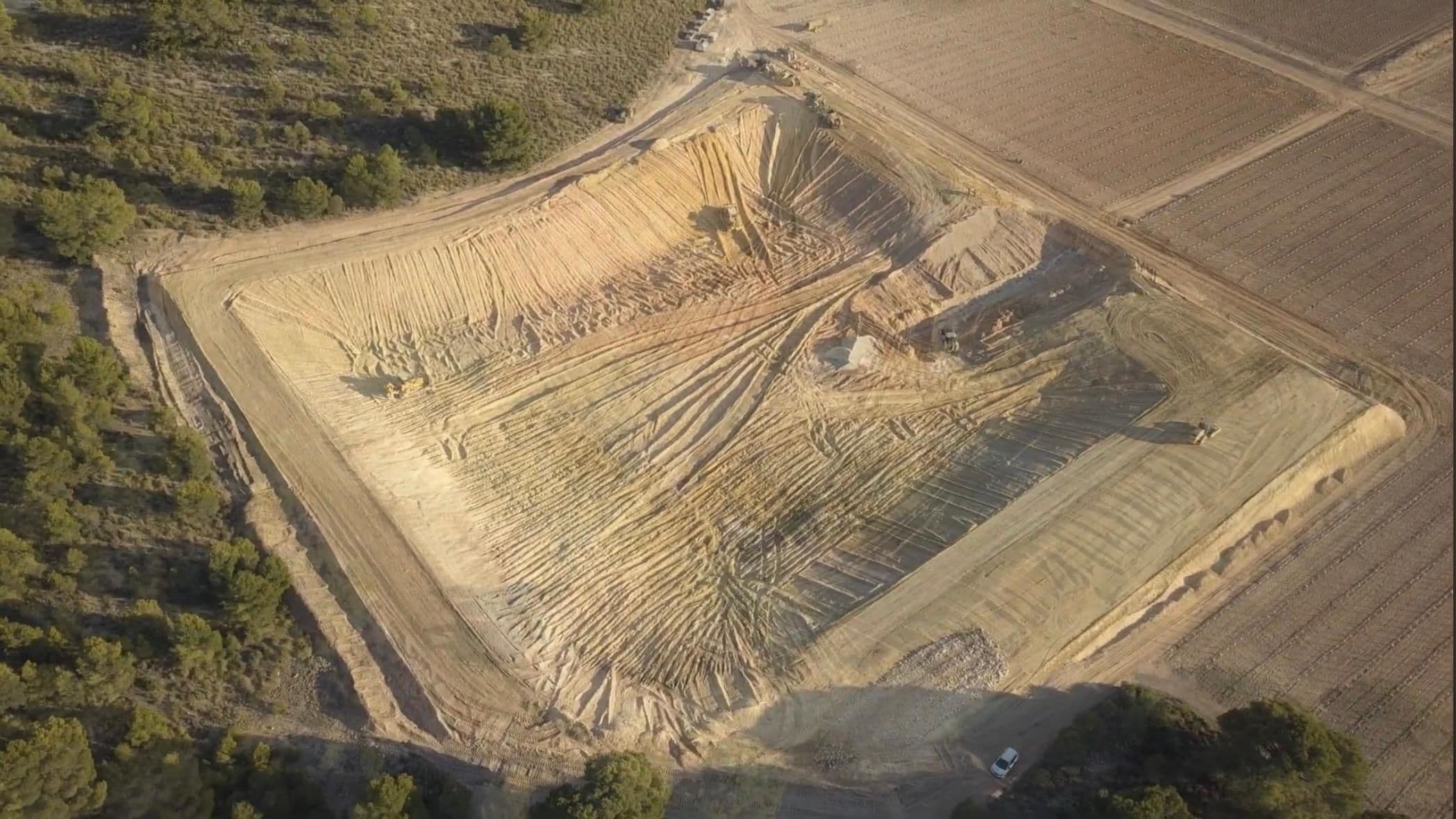La excavación avanzada, con el fondo del vaso todavía en rampa y una máquina refinando el talud del fondo