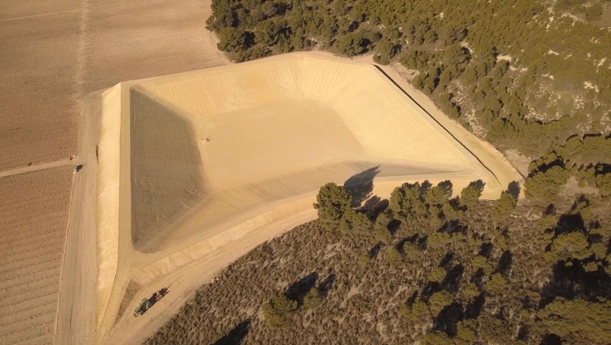 La balsa terminada a la luz de la tarde, con un tractor parado en la pista de coronación y el pinar al fondo